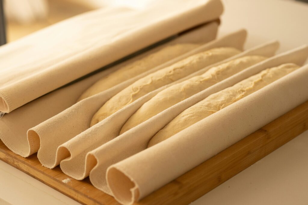 Close-up of baguette dough, shaped, on a wooden board, ready to bake.