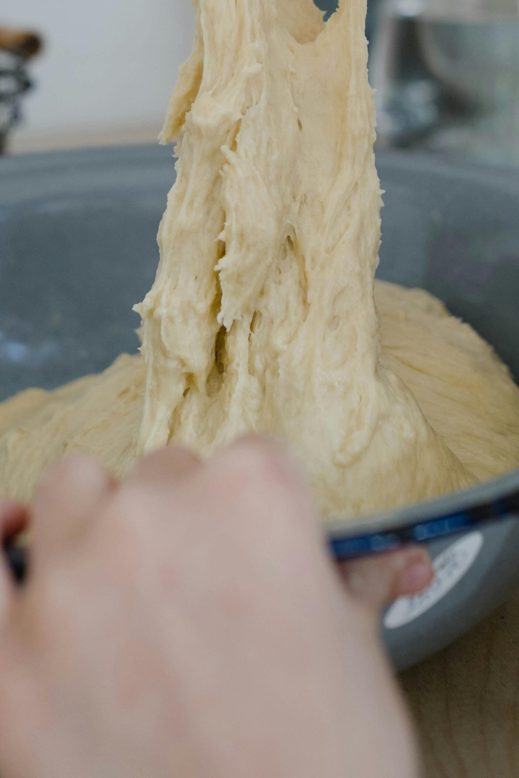 Close-up of hands kneading sticky dough in metal bowl, perfect for bakery-themed stock images.