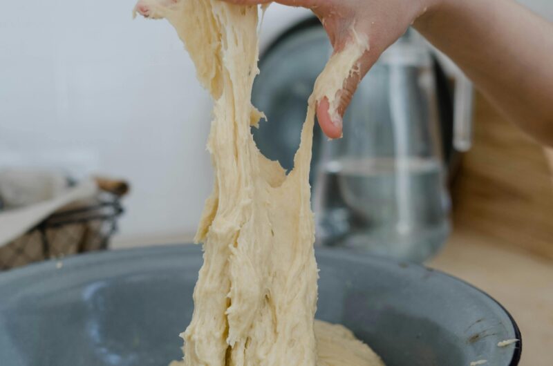 Close-up of hands kneading sticky dough in metal bowl,